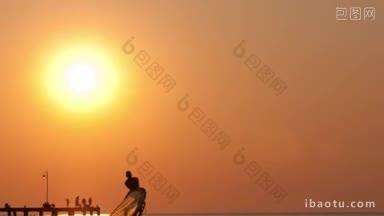 日落时分，平静的海面上，映衬着蔚为壮观的橙黄色天空，男子举起帆板或帆板